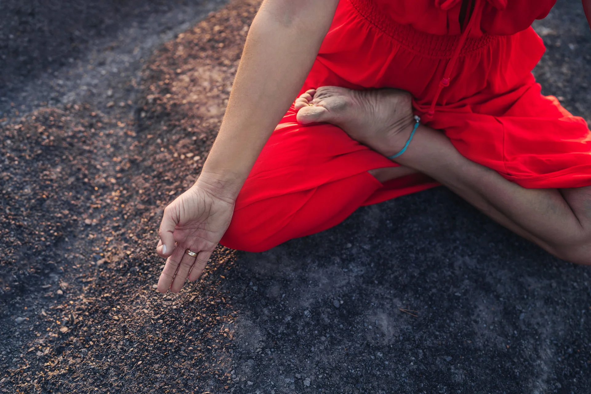 Detail ruky a nohou v meditačním sedu, v červených šatech na skále